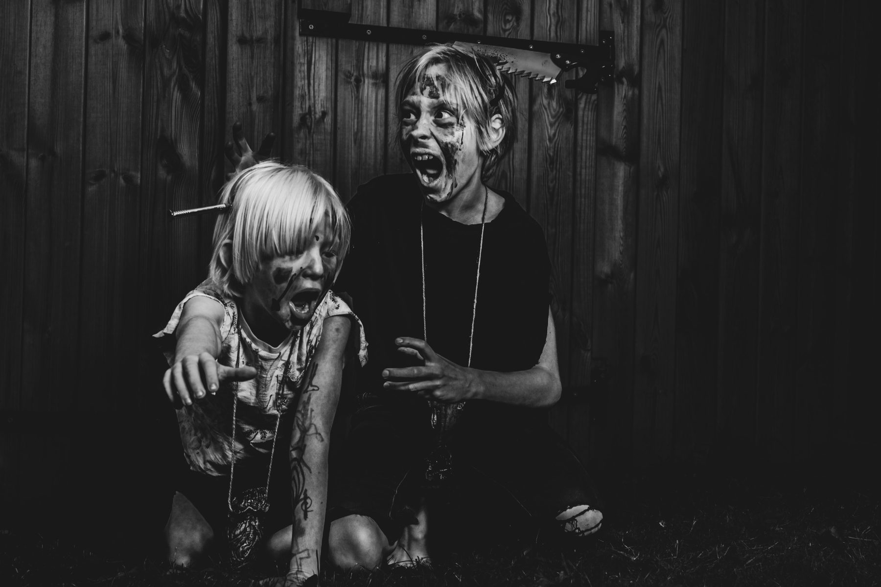 Two zombie kids crouched against a dark wooden fence.