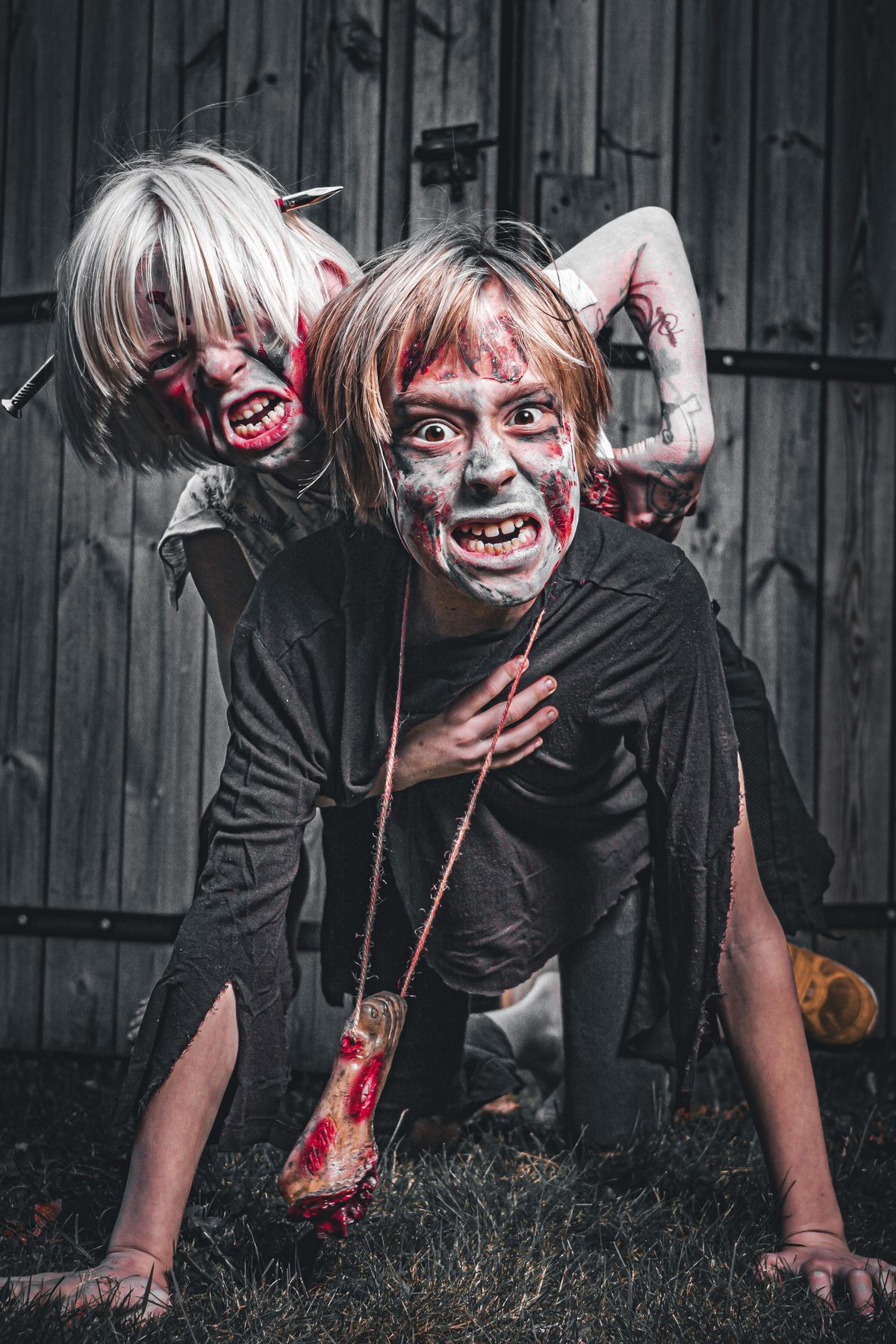 Two zombie kids crawling over each other on the grass, bloodied.