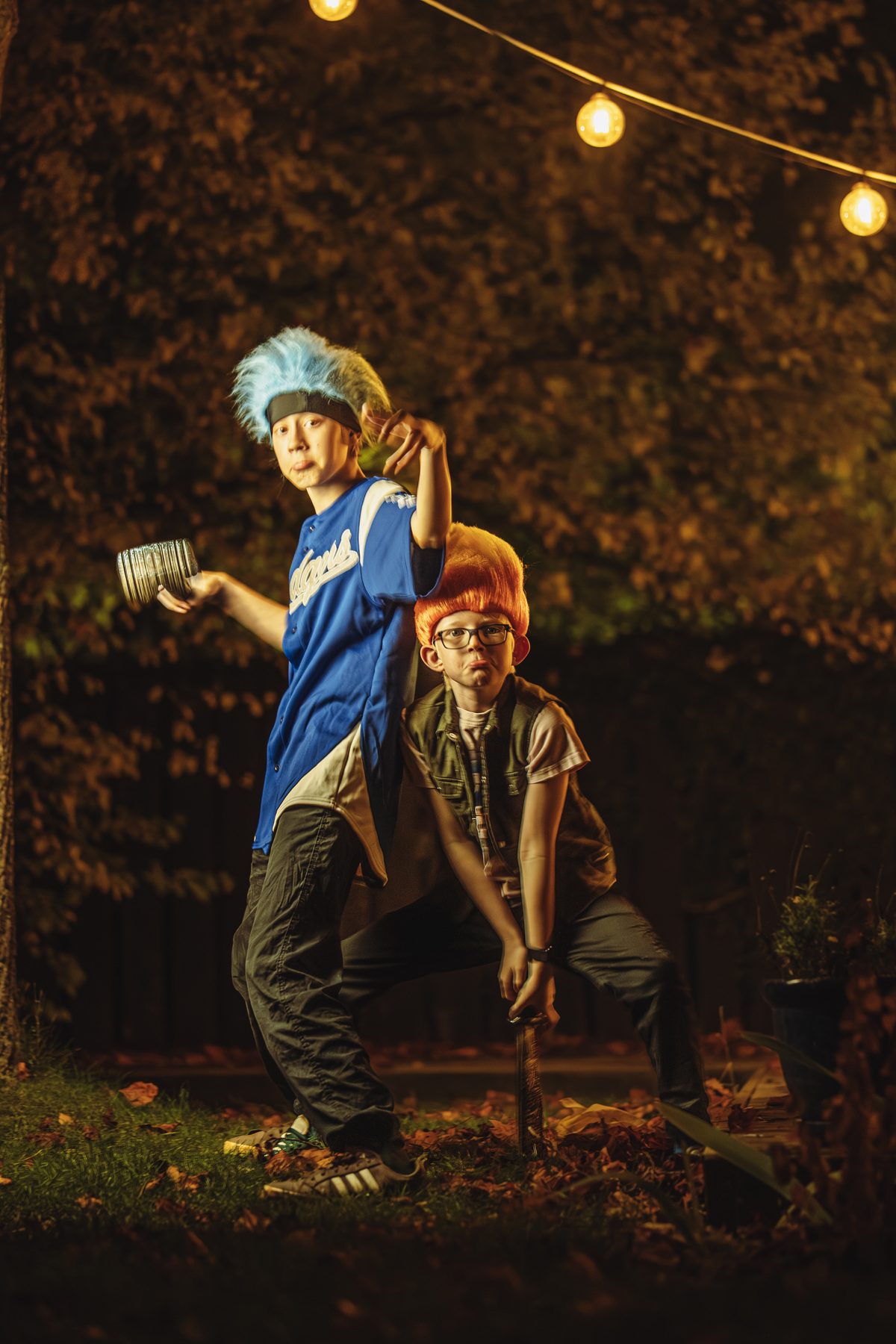 Blue troll winding up a throw, orange troll crouched with a sword under the string lights.