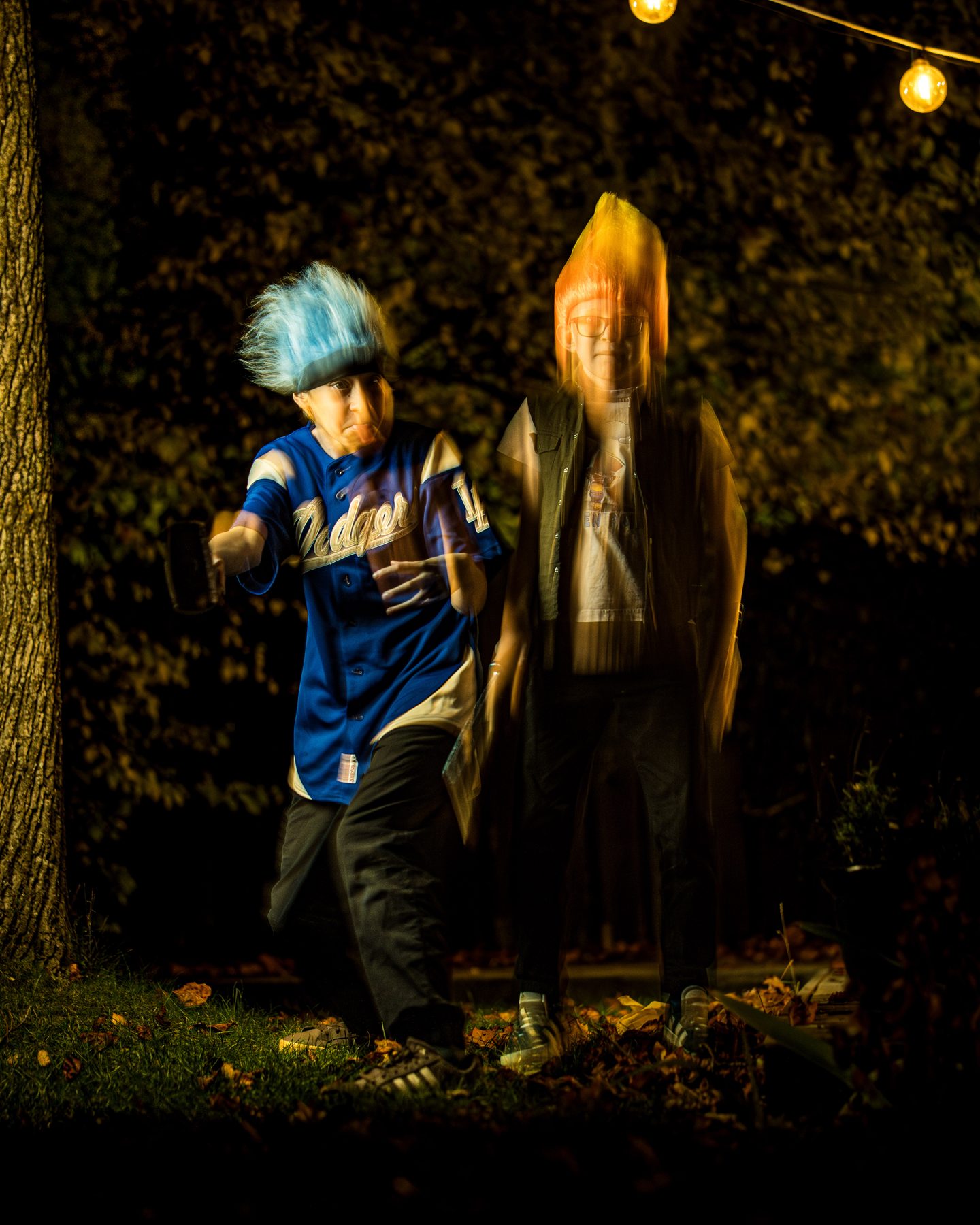 Two trolls in a dark backyard, one blue-haired and swinging, the orange one a glowing ghost.